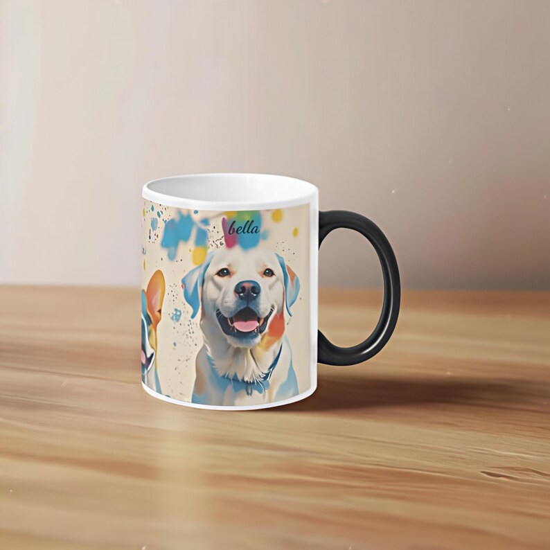 May include: White ceramic mug with a black handle. The mug features a colourful illustration of two dogs, one with the name "bella" written above it. The background is a light beige with colourful paint splatters.