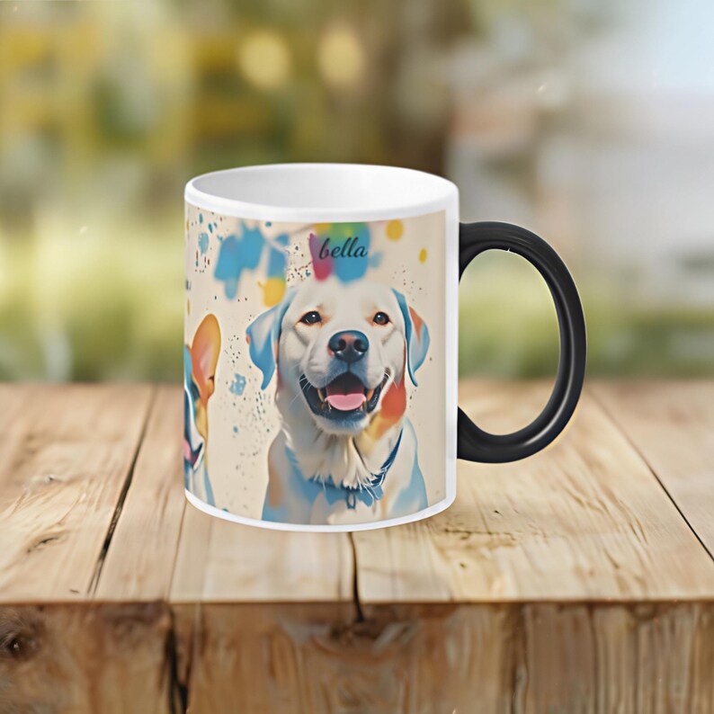 May include: White ceramic mug with a black handle. The mug features a colourful illustration of two dogs, one with the name "bella" printed on the mug. The background is a light beige with colourful paint splatters.