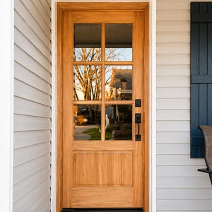 May include: A wooden front door with a glass paneled top section and a solid bottom section. The door has a black handle and is set in a white frame. A black doormat sits at the base of the door.