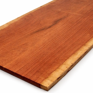 May include: A rectangular, reddish-brown wooden slab with a natural edge. The wood grain is visible, and the edges are a lighter tan color. This piece could be used for a variety of woodworking projects.