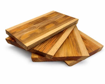 Puede incluir: Una pila de tablas de cortar rectangulares de madera. Las tablas son de madera marrón clara y oscura con vetas visibles. Las tablas están dispuestas en una configuración ligeramente en abanico, con los bordes visibles.