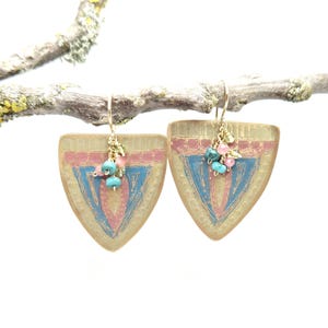 May include: A pair of gold tone earrings with a geometric design in shades of pink, blue, and gold. The earrings are shaped like a triangle and have a cluster of pink and turquoise beads dangling from the bottom.