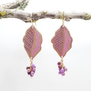 May include: A pair of gold earrings with a pink leaf design and a cluster of purple gemstones dangling from each earring.