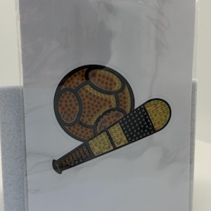 Puede incluir: Una pegatina con un dise&ntilde;o de b&eacute;isbol y bate. La pelota de b&eacute;isbol es marr&oacute;n con un patr&oacute;n de peque&ntilde;as formas amarillas y marrones. El bate es negro y amarillo con un patr&oacute;n texturizado. La pegatina est&aacute; en una tarjeta blanca.