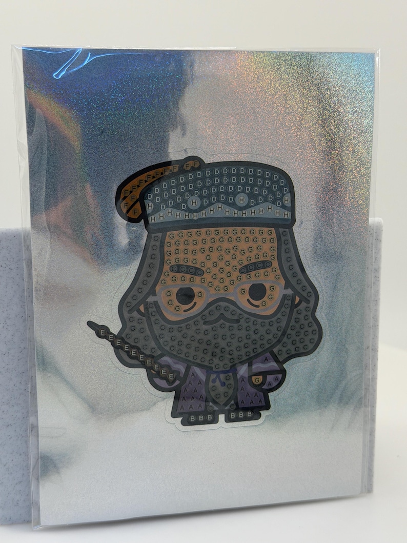 Puede incluir: Una pegatina con una imagen de dibujos animados de un mago con una larga barba y una varita. La pegatina tiene un fondo hologr&aacute;fico y est&aacute; encerrada en una funda de pl&aacute;stico transparente. El mago lleva un sombrero y una t&uacute;nica.