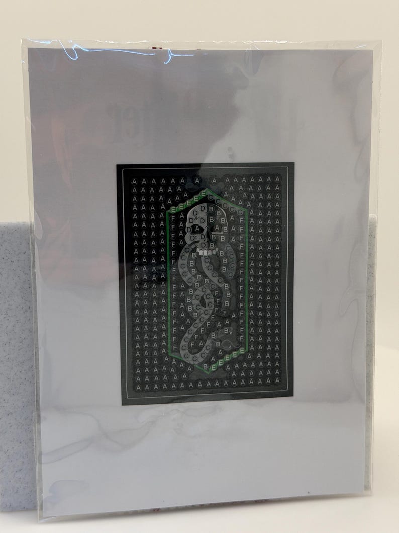 Puede incluir: Una impresi&oacute;n art&iacute;stica enmarcada con un fondo negro y un patr&oacute;n repetido de la letra "A". El emblema central, con borde verde, muestra una serpiente estilizada y las letras "B", "C", "D", "E" y "F".