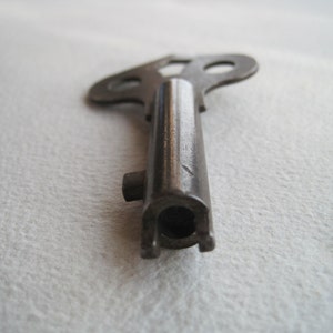 May include: A vintage metal key with a unique, three-pronged head. The key is made of a dark metal and has a worn, aged appearance.
