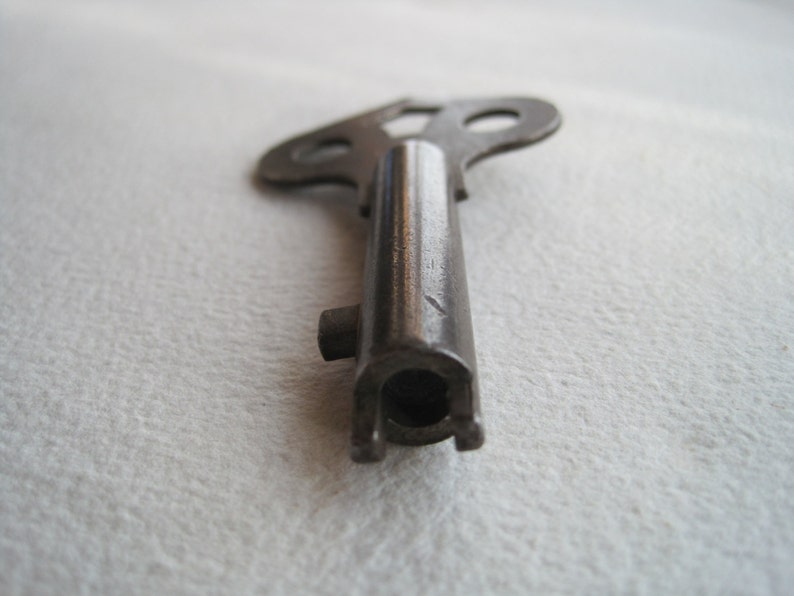 May include: A vintage metal key with a unique, three-pronged head. The key is made of a dark metal and has a worn, aged appearance.