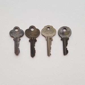 May include: Four antique keys with different designs and markings. The keys are made of brass and have a worn, aged appearance. The keys are arranged in a row on a white background.