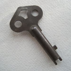 May include: A vintage metal key with a unique, irregular shaped head featuring three holes. The key is made of a dark, aged metal and has a long, straight shaft.