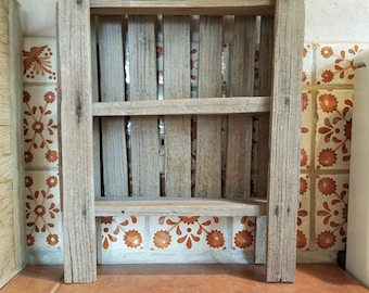 May include: A small, rustic wooden shelf with a picket fence design. The shelf has two horizontal slats and a slatted back, all made of weathered wood. The shelf is set against a backdrop of patterned tiles and a terracotta-colored surface.