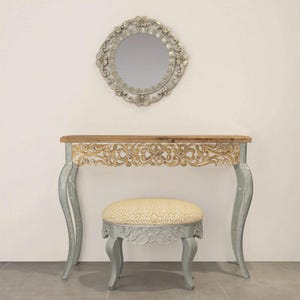 May include: A vanity set with a carved wooden table and stool. The table has a light blue finish and a carved wooden top. The stool has a light blue finish and a beige fabric seat. The mirror is round and has a silver frame with carved details.