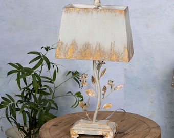 Puede incluir: Lámpara de mesa blanca con acabado de hoja de oro y una pantalla de tela blanca. La base de la lámpara presenta un diseño floral con hojas y rosas.