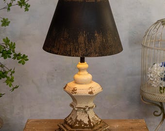May include: A distressed white and brown wooden table lamp with a black fabric lampshade. The lampshade has a distressed finish and is slightly angled.