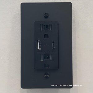 May include: Black electrical outlet with two USB ports and a standard outlet. The outlet is mounted on a black metal plate with the text "METAL WORKZ HARDWARE" below it.