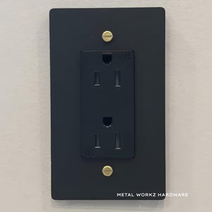 May include: Black metal electrical outlet cover with two brass screws. The outlet is labelled "1R".