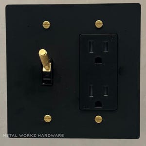May include: Black metal electrical outlet and light switch plate with a brass toggle switch and brass screws. The plate has the text "METAL WORKZ HARDWARE" at the bottom.
