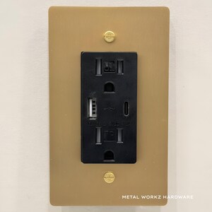 May include: A gold metal wall plate with a black electrical outlet and two USB ports. The outlet has the text "LEGRAND - GFCI OUTLET" printed on it. The plate has the text "METAL WORKZ HARDWARE" printed on the bottom.
