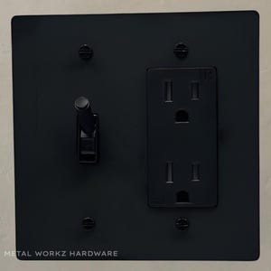 May include: Black metal electrical outlet and light switch plate with two screws on each side. The plate has the text "METAL WORKZ HARDWARE" at the bottom.