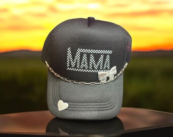 May include: Black trucker hat with a white checkered "MAMA" design, a silver chain, and a silver heart charm.