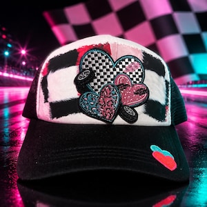 May include: A black and white trucker hat featuring a front panel with a black and white checkered pattern and a cluster of three heart-shaped patches. The patches include a checkered heart, a pink heart, and a teal heart with tire accents.