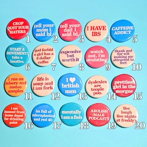 Puede incluir: Una colección de veinte botones redondos y coloridos con varias frases y declaraciones humorísticas en texto blanco. Los botones están dispuestos sobre un fondo azul claro, ofreciendo una estética lúdica y peculiar.