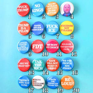 Op de afbeelding: Een verzameling van twintig kleurrijke politieke buttons met verschillende slogans. De ronde buttons tonen tekst in verschillende kleuren, waaronder rood, blauw, geel en oranje. De buttons drukken meningen uit over actuele gebeurtenissen.