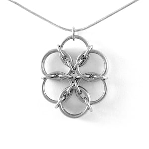 May include: A silver-colored necklace featuring a pendant shaped like a six-petal flower. The pendant is made of interconnected rings, suspended from a delicate chain. The jewelry is displayed against a white background.