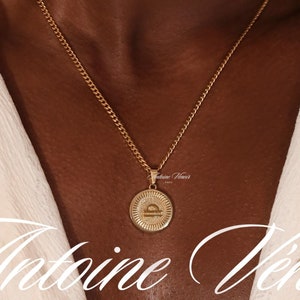 May include: A gold chain necklace with a gold pendant featuring the Libra zodiac symbol. The pendant has the text "Antoine Venir Paris" on it. The necklace is worn by a person with brown skin. The image includes the text "WATER-PROOF", "HEAT-PROOF", and "SWEAT-PROOF".