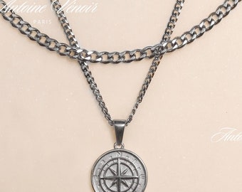May include: A silver chain necklace with a compass pendant. The necklace is layered with two chains, one thicker than the other. The compass pendant has a black and silver design.