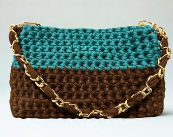 May include: A teal and brown crochet handbag with a gold chain strap. The bag is rectangular, with the top half in teal and the bottom half in brown. The gold chain strap provides a stylish contrast to the textured crochet.