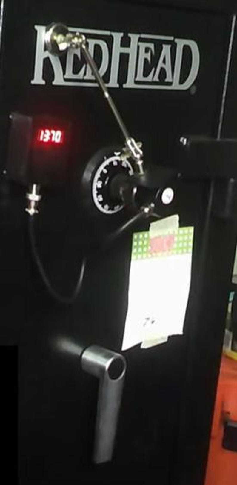 May include: Black safe with the word "REDHEAD" in white lettering. The safe has a digital display showing "1370". It features a combination dial, a handle, and a silver-coloured arm.
