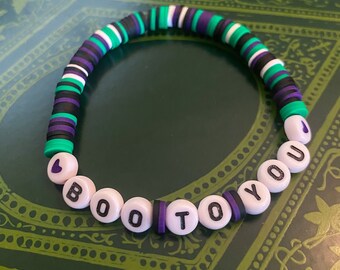 May include: A beaded bracelet with the words "I BOO TO YOU". The bracelet features a mix of white, black, green, and purple beads. The beads are arranged in a circular pattern, creating a fun and festive accessory.