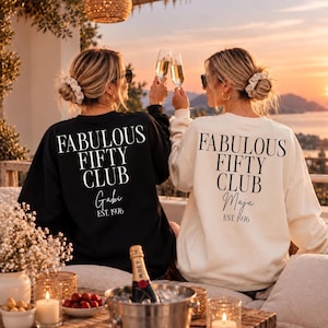 Könnte beinhalten: Ein schwarzes Sweatshirt und ein weißes Sweatshirt, jeweils mit dem Text FABULOUS FIFTY CLUB in Serifenschrift, sowie den Namen Gabi oder Maja und dem Text EST. 1976 in Schreib- und serifenloser Schrift auf der Rückseite der Kleidungsstücke.
