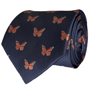 May include: A rolled navy blue tie featuring a repeating pattern of orange butterflies. The butterflies have detailed wing patterns and are evenly spaced across the tie's surface. The tie is made of a ribbed fabric.