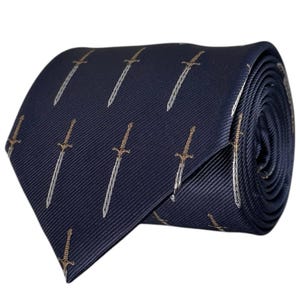 Puede incluir: Una corbata de color azul marino oscuro con un patrón repetitivo de pequeñas espadas bordadas en plata y oro. La tela tiene una sutil textura acanalada en diagonal, y la corbata se muestra enrollada para exhibir el patrón y el extremo puntiagudo.