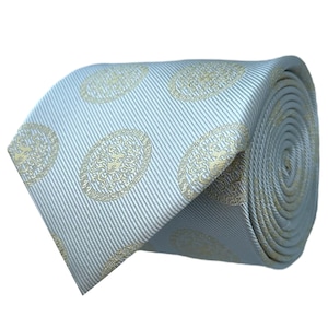May include: A light blue tie with a repeating pattern of gold-colored oval medallions. The tie is rolled up, showing the pattern and texture of the fabric. The medallions feature a detailed design, adding a touch of elegance to the accessory.
