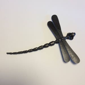 Puede incluir: Una escultura de libélula de metal negro con un cuerpo segmentado y alas detalladas.