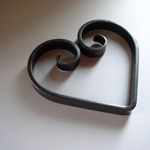 Puede incluir: Un diseño en forma de corazón de metal negro con dos espirales decorativos.