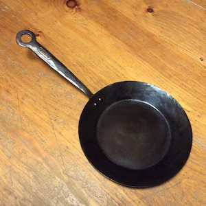 May include: A black cast iron skillet with a round handle. The handle has a small loop at the end and the word "MATFER" is stamped on the handle.