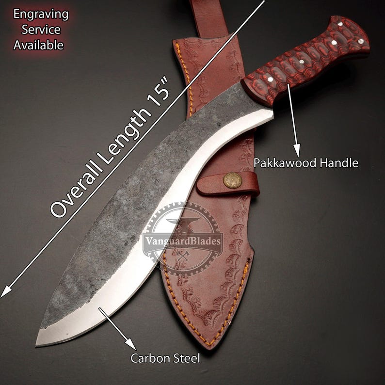 May include: A 15-inch overall length carbon steel kukri knife with a Pakkawood handle, displayed with a brown leather sheath. The knife has a curved blade and a dark, textured finish. The text "Engraving Service Available" is visible.
