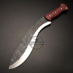 May include: A large, curved blade knife with a dark, textured finish. The handle is a deep red with white accents. The blade has a polished edge and a curved shape, suitable for various cutting tasks.