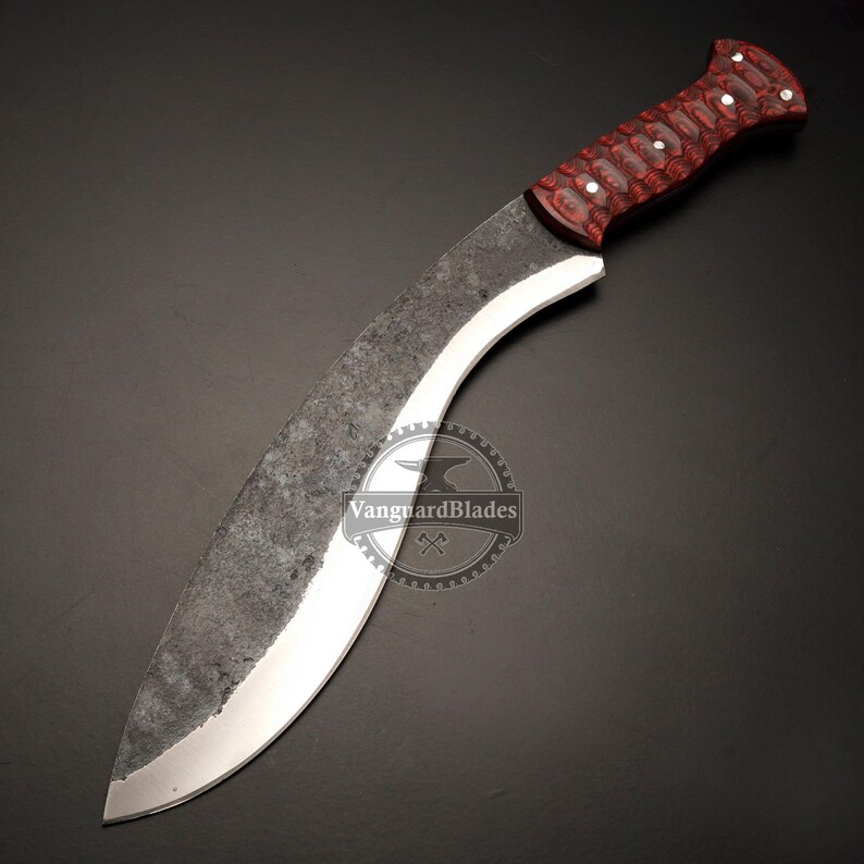 May include: A large, curved blade knife with a dark, textured finish. The handle is a deep red with white accents. The blade has a polished edge and a curved shape, suitable for various cutting tasks.