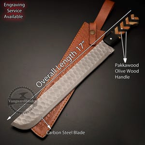 May include: A 17-inch carbon steel blade with a pakkawood olive wood handle. The blade has a hammered finish and is in a brown leather sheath.