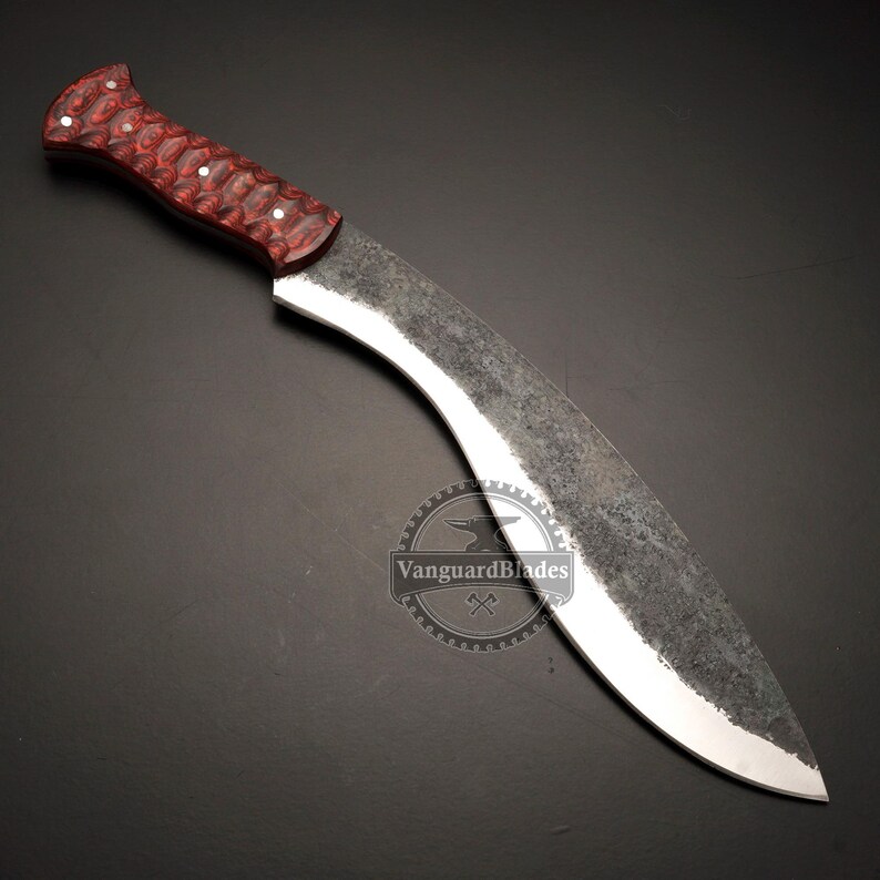May include: A large, curved blade knife with a red and brown patterned handle. The blade has a dark, textured finish with a polished edge. The knife is designed with a traditional shape and is likely used for cutting.