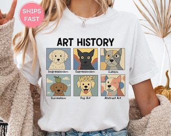 May include: White t-shirt with the text "ART HISTORY" above six dog illustrations representing art movements like Impressionism and Cubism. The Pop Art dog has a "WOOF!" speech bubble.