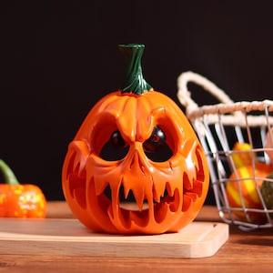 Peut inclure: Une citrouille d'Halloween orange avec un visage sculpté, des yeux noirs et une tige verte. La citrouille est posée sur une planche à découper en bois. Une petite citrouille et un panier avec des courges sont en arrière-plan.