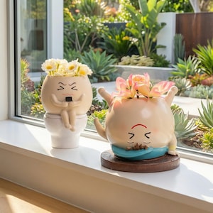 May include: Two quirky ceramic plant pots, one seated on a toilet and the other in a yoga pose, each filled with flowers. The beige pots have cartoon faces and sit on a windowsill, with a garden visible in the background.