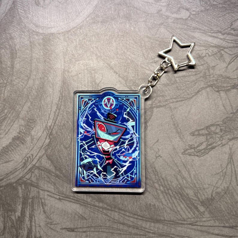 May include: A rectangular acrylic keychain featuring a cartoon character with a red and blue color scheme. The character is set against a blue background with white lightning-like patterns. A silver star-shaped charm is attached.