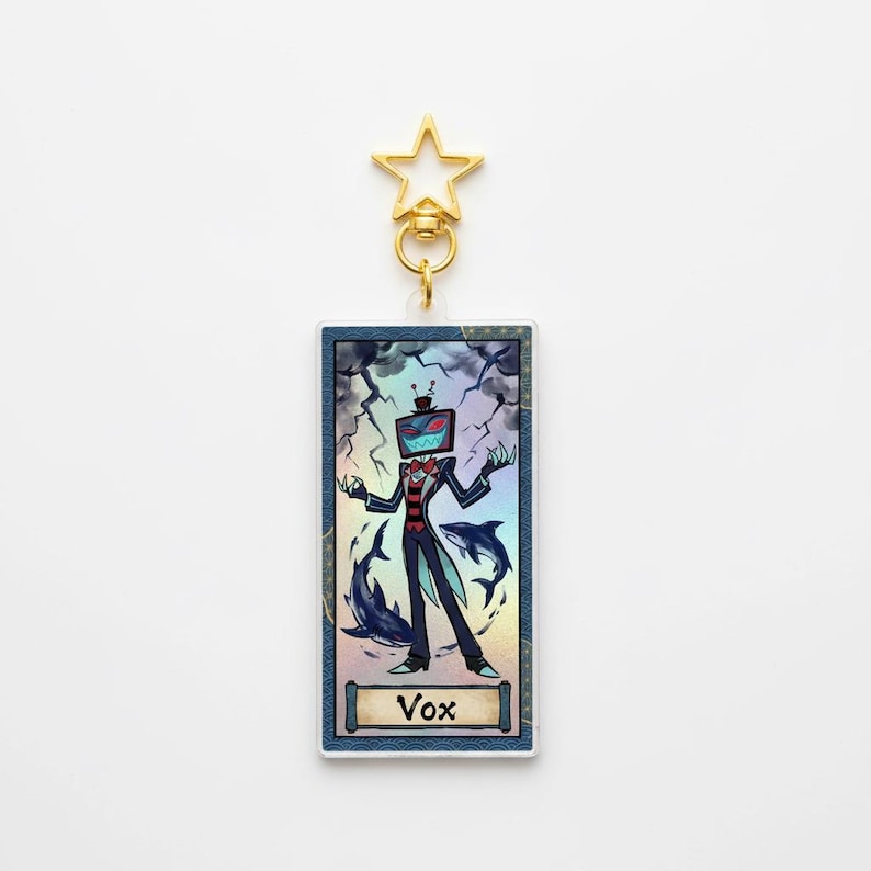 May include: A rectangular Vox keychain with a gold star-shaped clasp. The image features a cartoon character with a TV head, a red suit, and a blue background with lightning and dolphins. The word "Vox" is at the bottom.